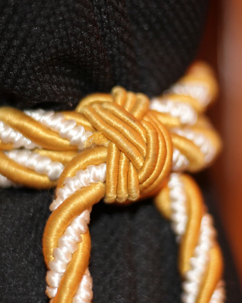 Cordão dourado e branco amarrado em nó numa cortina preta
