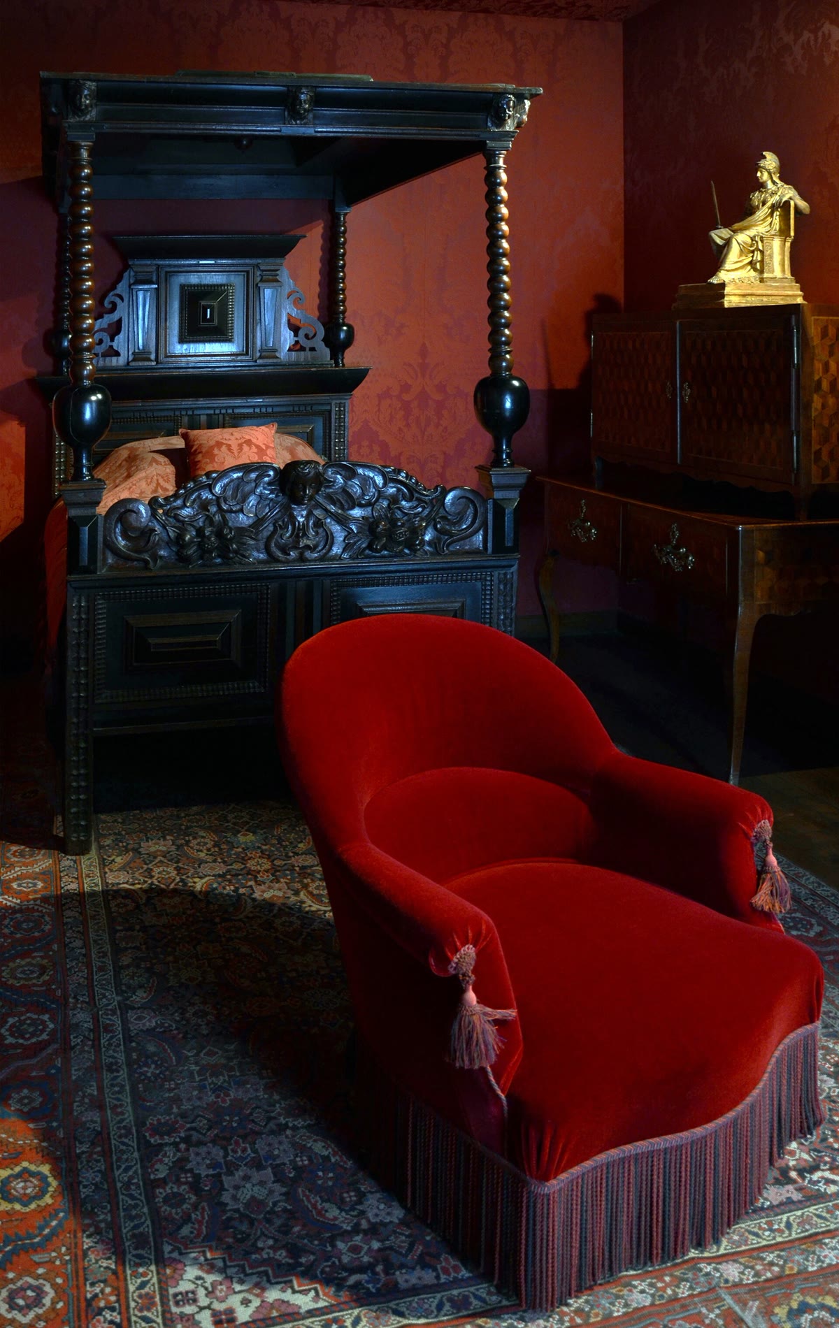 Quarto à meia-luz com cama de dossel escura e poltrona de veludo vermelho